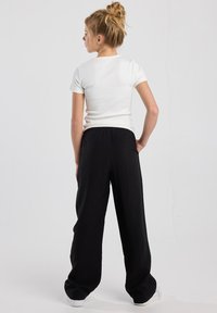 White short-sleeve top paired with loose-fitting black pants. The outfit has a relaxed fit and elastic waistband, with smooth fabric texture.