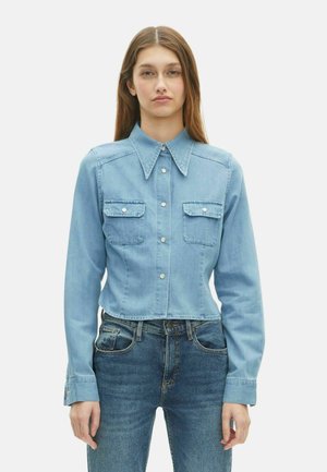 Lichtblauwe denim cropped shirt met een gekraagde halslijn, lange mouwen, twee borstzakken en drukknoopsluitingen. Glad textuur met gestikte details.