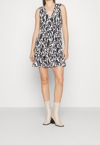 Abito con stampa leopardata in bianco e nero, dotato di scollatura a V profonda, orlo arricciato e senza maniche, abbinato a stivaletti beige con tacco.
