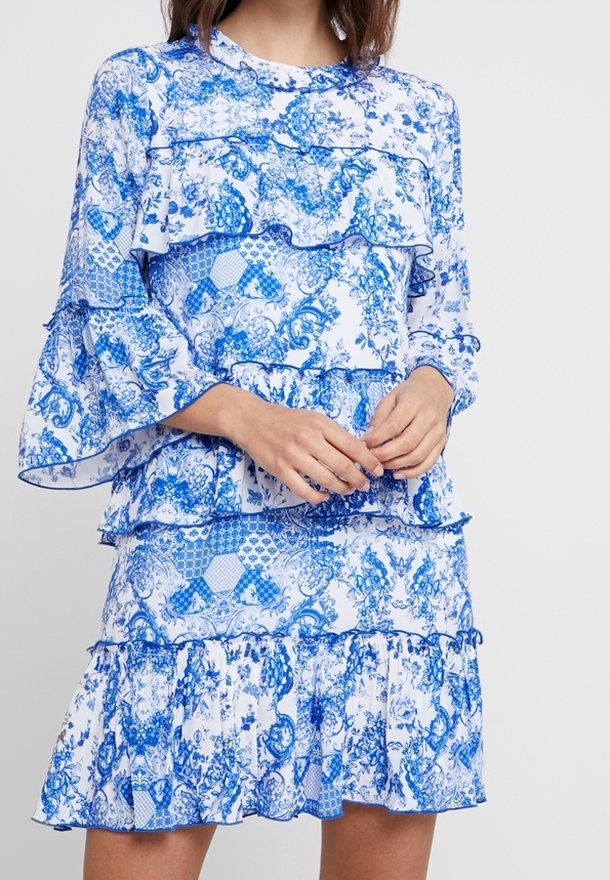 Vestido con estampado floral y volantes en capas, que presenta una combinación de colores azul y blanco, manga larga y escote redondo.