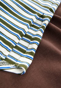 Nahaufnahme von gefaltetem Stoff mit olivgrünem, weißem und blau gestreiftem Textil über glattem braunem Textil.