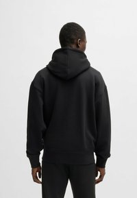 Czarna bluza z kapturem o dużym, regulowanym kapturze, z ściągaczami na rękawach i luźnym kroju, wykonana z gładkiej tkaniny bawełnianej.