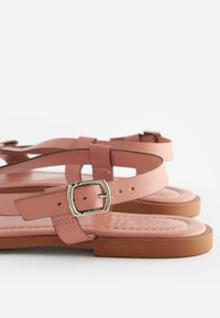 Rosa Leder-Sandalen mit flacher Sohle, ausgestattet mit mehreren übereinanderliegenden Riemen und einem silberfarbenen Schnallen-Detail. Glatte Textur mit einem eleganten Design.