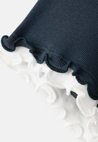 Prim-plan al unui țesătură ribbed navy și alb, cu margini ondulate și tivuri scallopate suprapuse.