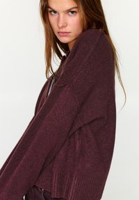 Bordó színű, túlméretezett pulóver bordázott mandzsettákkal és szegéllyel, dombornyomott kötött mintával. Hosszú ujjú, laza szabású.