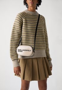 Maglione a righe beige e oliva, con polsini a costine. Gonna khaki plissettata. Piccola borsa a tracolla color crema con il logo "KARL LAGERFELD JEANS".