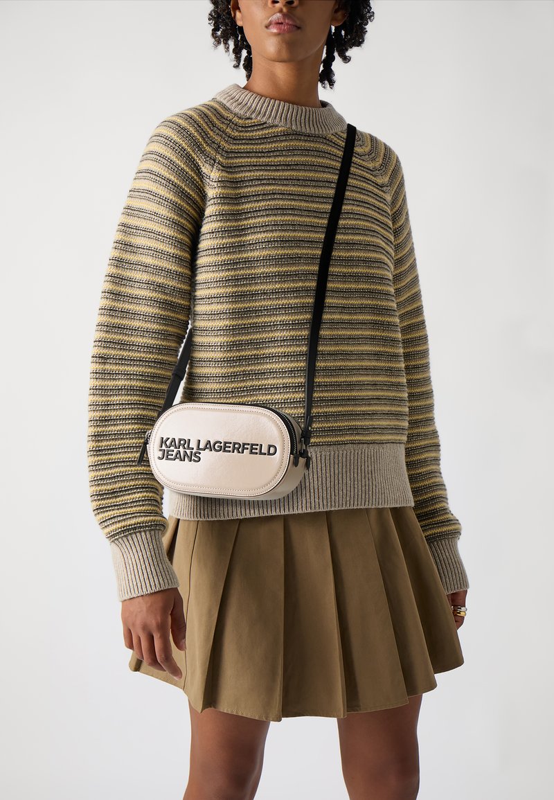 Maglione a righe beige e oliva, con polsini a costine. Gonna khaki plissettata. Piccola borsa a tracolla color crema con il logo "KARL LAGERFELD JEANS".