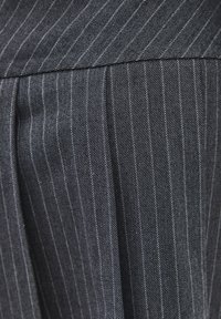 Sort stof med smalle striber og en tekstureret vævning, der har tynde hvide linjer, som løber lodret, designet til at skabe et skræddersyet udseende.