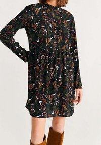 Langärmliges schwarzes Kleid mit einem Paisleymuster in Grüntönen, Orange und Pink; es hat eine geraffte Taille und eine weiche Stofftextur.