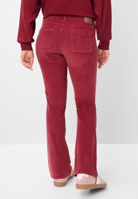 Rode corduroy flarebroeken met twee achterzakken, textuurstof en een tan merklabel op de tailleband. Gecombineerd met lichtroze schoenen.