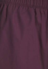 Violetti kangas, jossa on sileä pinta ja joustava vyötärö; siinä on hienovarainen kiilto ja pehmeä laskostus, korostaen sen kevyttä laatua.