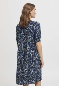 Mornarsko modra obleka z cvetličnim vzorcem v zeleni in beli barvi, kratkimi rokavi in sproščenim krojem do kolen. Gladka tekstura tkanine.