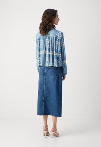 Blå mønstret bluse med samlet detalj, parret med et langt denimskjørt og hvite stroppesandaler. Antrekket har en avslappet passform.