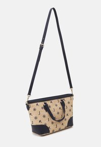 Sac fourre-tout tissé beige avec des accents en simili cuir bleu marine, deux poignées, une bandoulière ajustable et des motifs floraux, doté d'une fermeture éclair.