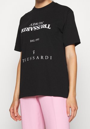 Black short-sleeve t-shirt made of cotton. Features white printed text: "TRUSSARDI NEW" and "DAL 1911" in varying fonts. Relaxed fit.