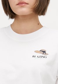 Hanorac alb din bumbac, cu un design brodat de pălărie de paie și textul "BI AZING" în negru, cu accente de albastru deschis.