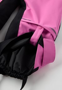 Vaaleanpunaiset ja mustat vedenpitävät ulkoiluhousut, joissa on joustavat hihnat ja heijastinraita; sileä pinta, nappikiinnitys ja taskusauma.