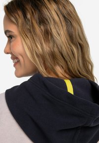 Felpa con cappuccio in pile navy con un accento giallo sul cappuccio. Presenta una forma rotonda e un tessuto a doppio strato, mostrata da una vista laterale.