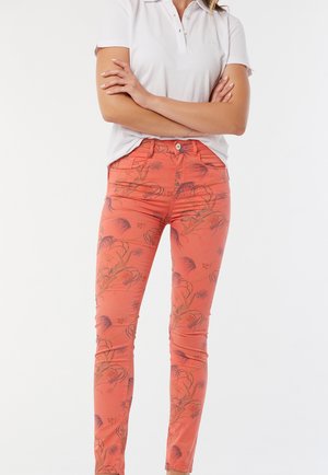 Pantalons corail avec un motif floral, coupe ajustée, taille boutonnée et passants de ceinture. Associés à un polo blanc, illustrant un style décontracté.