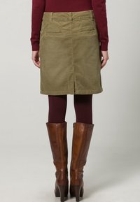 Olijfgroene corduroy rok met achterzakken, tot op de knie, met een achterventilatie. Gepaard met bruin leren kniehoge laarzen.