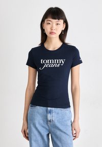 Námořnická modrá přiléhavá tričko vyrobené z bavlny, s bílým logem "tommy jeans" na přední straně. Krátké rukávy a kulatý výstřih.