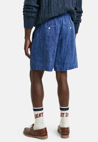 Shorts in lino blu navy con un fit rilassato, caratterizzati da due tasche posteriori e bottoni bianchi, abbinati a scarpe marroni e calze bianche a coste.