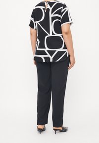 Czarna i biała góra z wyrazistymi geometrycznymi wzorami, krótkimi rękawami i detalem z kluczykowym wycięciem z tyłu; połączona z luźnymi czarnymi spodniami i butami w kropki.