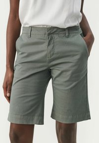 Shorts vert clair en tissu mélange coton, avec poches latérales, passants pour ceinture et coupe droite avec un ourlet au-dessus du genou.