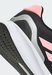 Baskets de sport noires avec une tige texturée, accents roses à l'arrière et sur le côté, et une semelle extérieur en caoutchouc blanc et adhérent. Détails en argent présents.