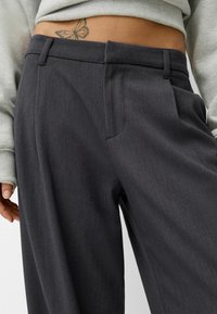 Pantaloni grigi su misura con una texture liscia, dotati di una tasca singola e una piega ben stirata lungo la parte anteriore.