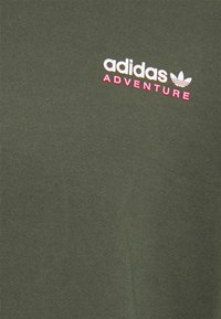 Oliveově zelené bavlněné tričko s ribbed texturou, se bílým a růžovým logem "adidas ADVENTURE" na přední straně.