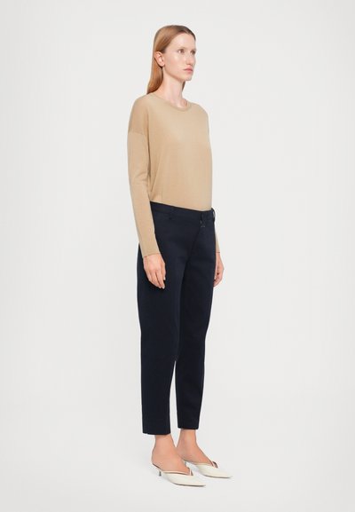 Beige langermet topp, marineblå smale bukser og off-white mules. Toppen har rund hals og løs passform. Buksene har sidelommer.