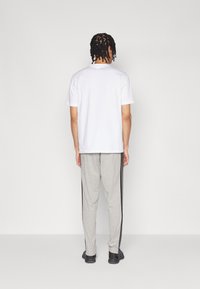Witte t-shirt met korte mouwen, gecombineerd met lichtgrijze joggingsbroek met zwarte zijstrepen. Persoon gezien van achteren.