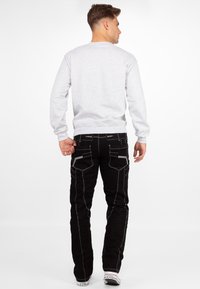 Felpa grigia con orlo e polsini a costine, abbinata a jeans neri con cuciture bianche e più tasche. Sneakers bianche completano il look.