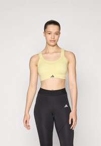 Gul sports-bh med scoop hals, tykke stropper og logo-detalj. Kombinert med svarte høytlivs leggings med sidesømmer.
