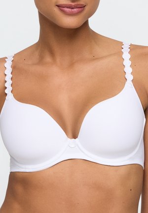 Vrouw draagt een witte beugelbeha met hartvormige getextureerde bandjes en een klein rond decoratief element aan de voorkant in het midden.
