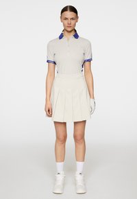 Polo grigio con dettagli blu, maniche corte e colletto, abbinato a una gonna plissettata color crema. Sneakers bianche e guanti completano il look.