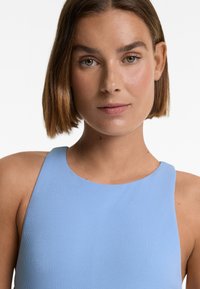 Light blue ribbed top with a round neckline and wide shoulder straps. Smooth texture and fitted design, showing upper body only.