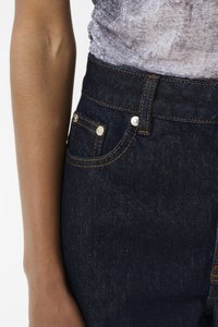 Mørkeblå denimjeans med kobbersting, høy midje og frontlommer med sølvnitter. Teksturen virker jevn og solid.