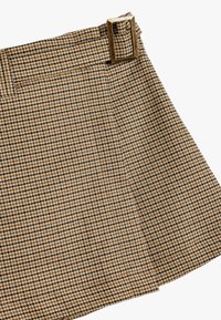 Hame kera ruskean ja mustan houndstooth-kuvion xäyn eli flare-mallisena, jossa on metallinen neliön muotoinen solki vyötäröllä. Teksturoitu kangas.
