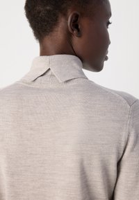Lys grå pullover med krave, der har en blød tekstur og subtil strikkemønster, viser bagsidevinklen og skulderdetaljerne.