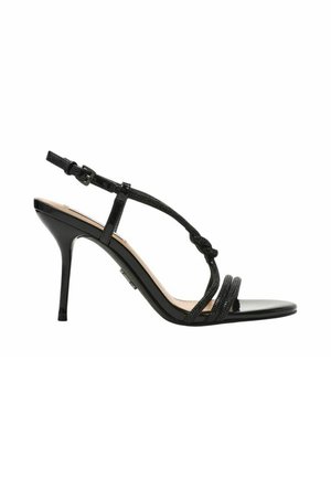 Sandalo nero con tacco alto, sottili cinturini, fibbia alla caviglia e dettaglio annodato davanti su sfondo bianco.