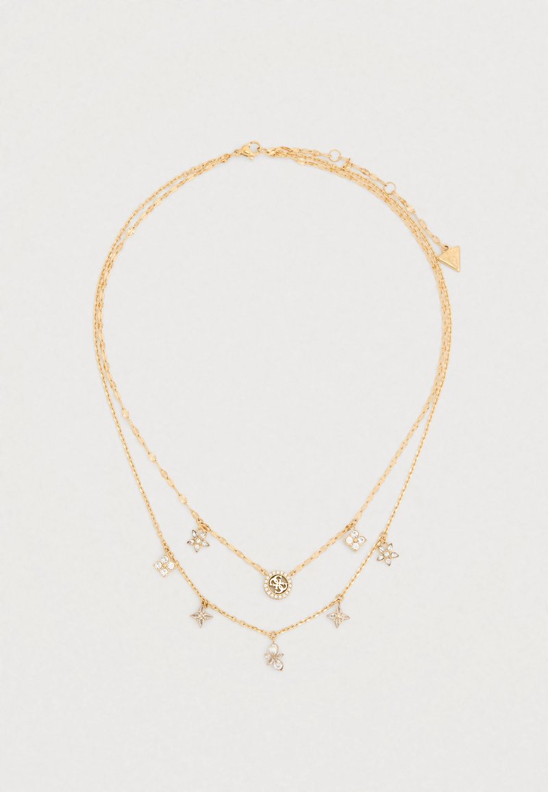 Χρυσό έθνικ κολιέ με τρία στρώματα αλυσίδων με διάφορα μενταγιόν, συμπεριλαμβανομένου ενός κυκλικού μενταγιόν και διακοσμητικών ανθικών σχημάτων.