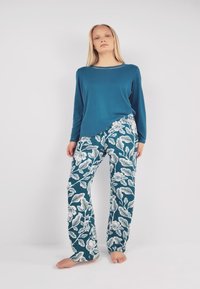 Teal long-sleeve top paired with loose-fitting, floral-patterned pants in blue and white, showcasing a smooth texture and relaxed design.