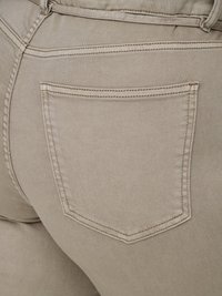 Gros plan sur un tissu en jean beige montrant la poche arrière et les détails de couture d'un pantalon.
