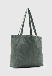 Zöld szövet táska két vállpánttal, téglalap alakú, és textúrált felülettel. Egyszerű, díszítetlen dizájnnal rendelkezik.