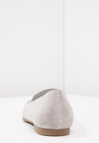Lichtgrijze suède platte schoen gezien vanaf de achterkant, met een ronde hak en een eenvoudig, elegant ontwerp tegen een witte achtergrond.