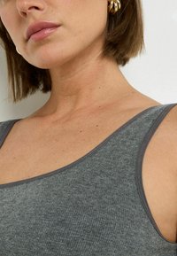 Canotta grigia a costine con spalline sottili e un bordo di un grigio scuro a contrasto, che presenta una texture morbida e una vestibilità rilassata.