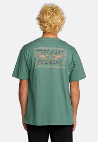 Groene katoenen t-shirt met een grote retro grafische print op de achterkant met bloemenaccenten, korte mouwen en een relaxte pasvorm.