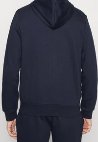 Sudadera de color azul marino hecha de una mezcla de algodón, con capucha con cordón, puños y dobladillo de canalé; textura suave y corte relajado.
